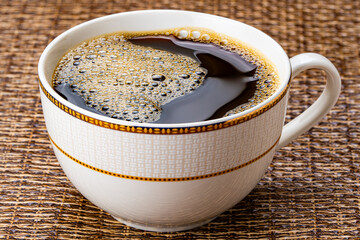 A cup of black coffee. High angle view of hot black coffee with air bubbles in beautiful brown ceramic cup on dark table mat.