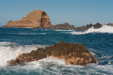 Porto Moniz Natural Swimming Pools waves with rocks and lighthouse in the background 