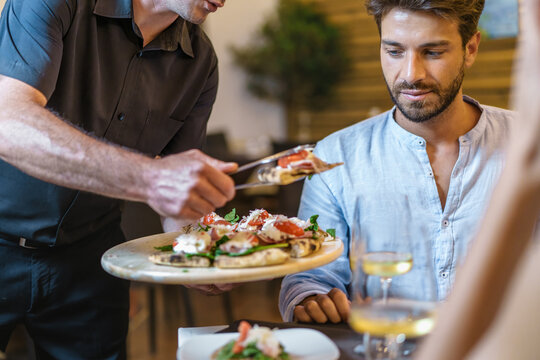 Waiter serving Italian appetizer to young man in restaurant - Authentic dining experience