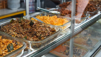Food stalls called warteg share a variety of buffet traditional menus of indonesia with vegetables, chicken curry sauce, beef, eggs, tofu, tempeh. Menu in glass display case. 