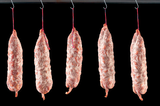 saucisson sec de Savoie suspendu aux crochets du boucher sur fond noir