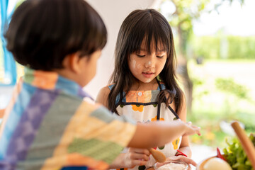 Two young children baking together in kitchen wearing aprons