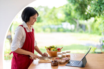 Asian woman cooking while looking at recipe on tablet computer