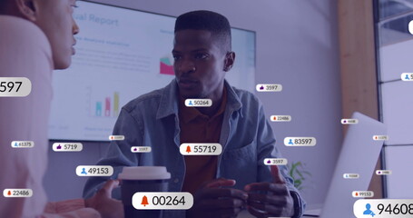 Image of social media icons with numbers over diverse colleagues discussing work in office