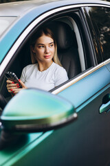 Young woman sitting in car and using mobile phone