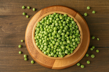 Fresh green peas in bowl on wooden table, top view