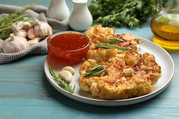 Delicious baked cauliflower steaks with sauce on blue wooden table