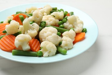 Tasty cooked cauliflower with green peas, string beans and carrot slices on white marble table, closeup