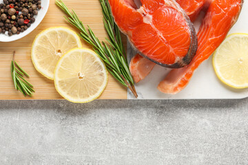 Board with fresh salmon steaks, peppercorns, rosemary and lemon on grey textured table, top view. Space for text