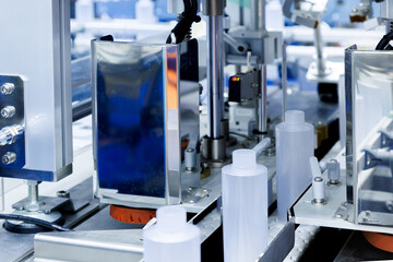 robot arm moving plastic bottle to conveyor belt of auto capping and labeling machine at cosmetic and skin care manufacturing. cosmetic industry and ai technology machinery concept.
