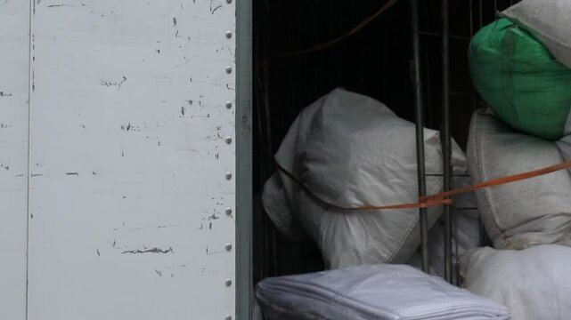 A truck driver with short hair loads a cart into his truck and closes the side door. He ensures everything is secure before hitting the road, ready for the next delivery.