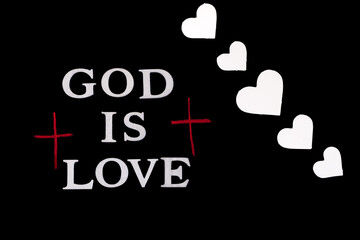 God Is Love written in silver lettering flanked by hand drawn crosses in red pastel pencil isolated on black background with flourish of white hearts. 