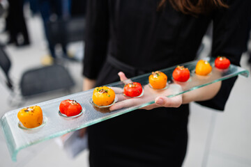 glass platter of small red and orange stuffed peppers being passed by caterer at outdoor event