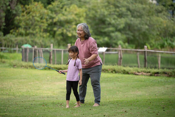 Fototapeta premium Happy Asian family children playing badminton with grandma in the park