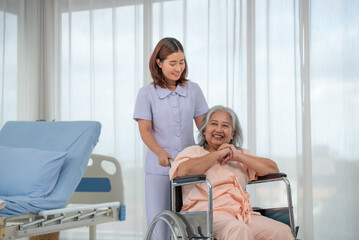 Obraz premium Asian nurse pushing senior female patient in a wheelchair at the hospital ward