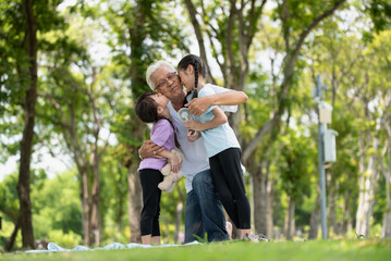 Happy Asian family children having fun and kissing her grandfather on the cheek in the park