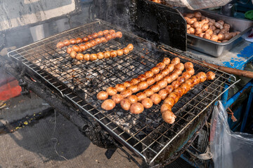 Grilled Pork and Rice Sausage or Northeastern sausage (Sai Krok Isan) on the grill with charcoal and smoke billowing. Thai street food are popular.