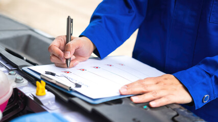 Close-up at a mechanic foreman's hand is checking on multi-point car service guideline checklist...