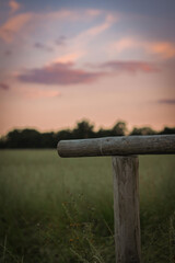 sunset over the field in summer with dramatic sky with wooden fence in front