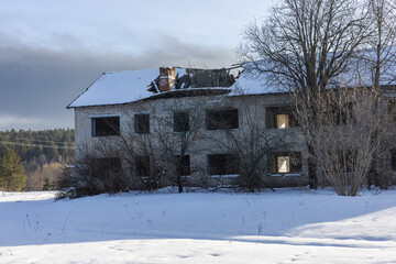 Abandoned building in a winter landscape, bathed in sunlight on snowy ground. Roof caved in, windows broken, telling a story of ruin and decay. Lonely and spooky, a reminder of the past.