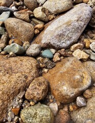 A serene beach scene featuring smooth pebbles and stones against a textured stone wall, capturing the natural beauty of gray and white hues along the shoreline