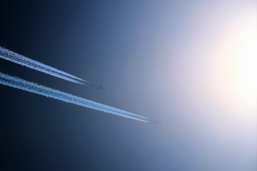 Two planes are flying towards the sun. Airplanes in the blue sky. Airplane with contrail.