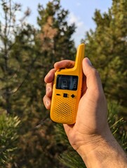 A yellow radio device held in hand in the forest.