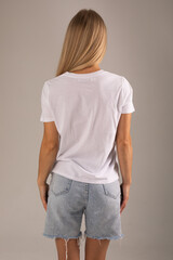 Obraz premium Blonde girl posing with her back on a white background in a white T-shirt and denim shorts