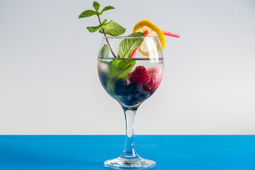 cocktail berry raspberry blueberry lemon and mint in a glass with a straw on a gray background