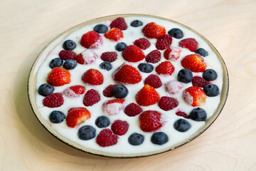In a plate with whipped cream, strawberries, raspberries and blueberries on the table.