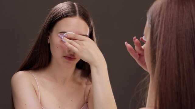 A young beautiful girl removes makeup with a cotton pad and micellar water from her face and eyes.