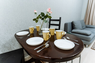 The dining table displays a lovely arrangement of plates, cups, utensils, and a beautiful vase filled with colorful flowers, creating a warm and inviting atmosphere in the room