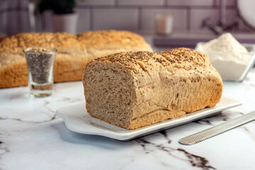 Homemade whole wheat bread with oatmeal and chia seeds and sesame seeds on kitchen table with ingredients 