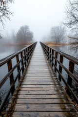 Naklejka premium A wooden bridge disappearing into the fog, spanning across a river shrouded in early morning mist