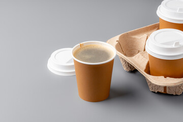 Warm coffee in a brown paper cup on a gray surface with a tray
