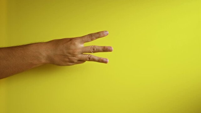 Man's hand showing three fingers against a vibrant yellow background, emphasizing counting, gesture, and communication in a colorful and expressive setting.