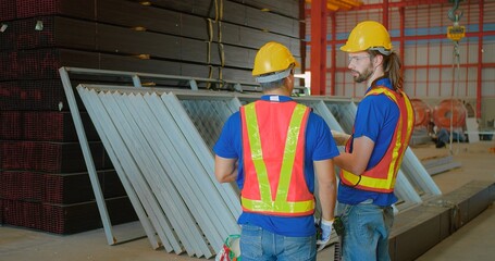 Two construction workers discussing plans inside a spacious warehouse. They are wearing safety gear, emphasizing teamwork and collaboration on the job site.