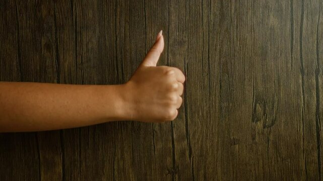 Woman hand showing thumbs up gesture against dark wood background portraying approval and satisfaction