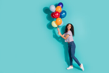 Full body photo of attractive young woman hold air balloons dressed stylish striped clothes isolated on aquamarine color background