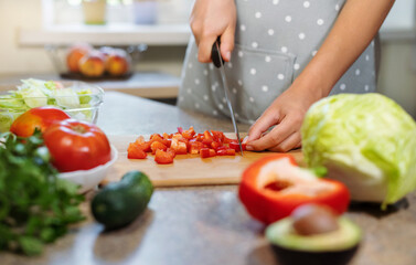 Closeup female hands slice red pepper of knife. Woman cooks healthy food in kitchen with vegetables for breakfast or lunch.