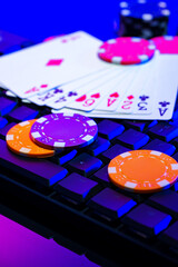 A vibrant arrangement of poker chips and playing cards on a gaming keyboard with a mouse at an online casino setup during the evening