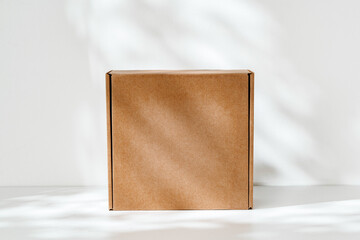Fototapeta premium Simple brown cardboard box positioned on a white surface with soft angled shadows in natural light