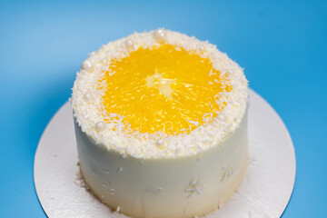 Delicious white cake decorated with orange and coconut flakes on blue background