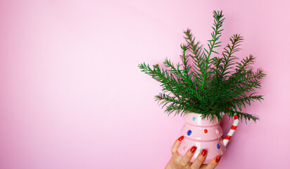 Womans hand is holding a christmas tree mug with branches, kitschy image on pink background