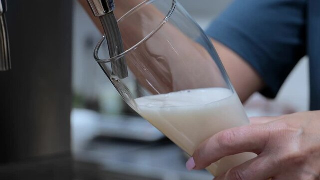 A woman pours beer. Strong, light, unfiltered beer, ready to drink. The bartender pours beer into a glass. Close-up of a bartender's hand filling a glass with light beer.