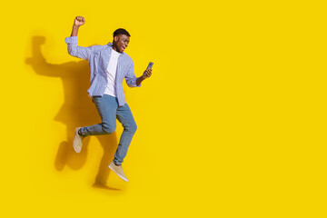 Fototapeta na wymiar Full length photo of handsome good mood guy wear plaid shirt jumping typing modern gadget emtpy space isolated yellow color background
