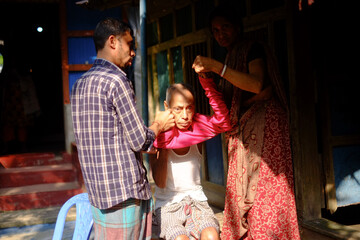 Bangladeshi family members helping sick old man in being dressed up 