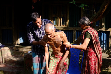 Bangladeshi family members helping sick old man in taking shower 