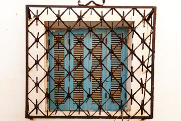 ventana con persianas de madera azules con reja decorativa oxidada como protección en una facha blanca