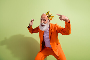 Portrait of funky eccentric grandfather point fingers crown wear orange suit isolated on green color background